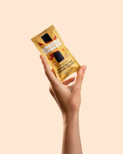A hand holding a Krack’d Snacks Peanut Butter Caramel Crunch bar with a clean label and crunchy texture.