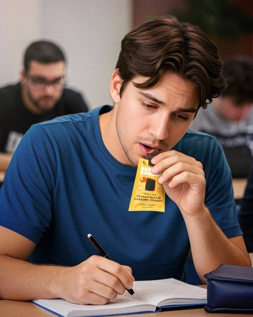 Young man in blue t-shirt eating Krack’d Snacks peanut butter caramel crunch bar while studying.
