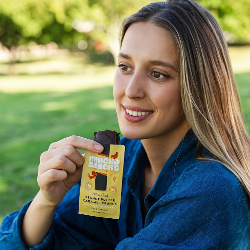 A woman holding a Krack'd Snacks Peanut Butter Caramel Crunch Bar, showcasing a keto-friendly snack for Mother's Day.