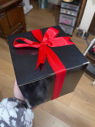 1. A black gift box from Krack’d Snacks tied with a bright red satin ribbon and a bow.