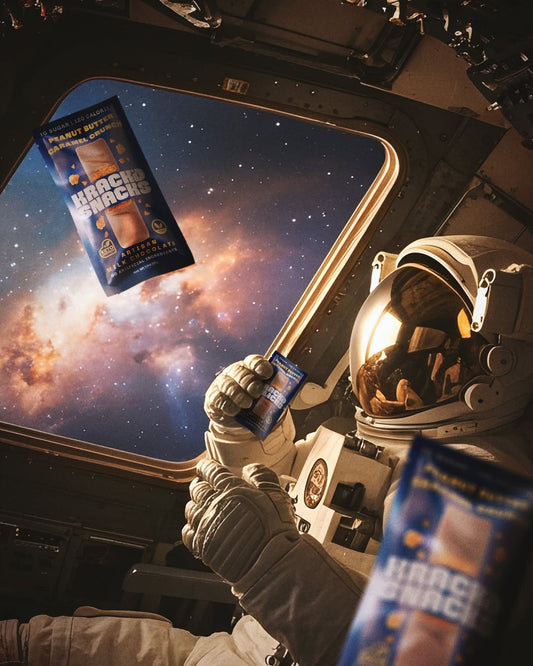 An astronaut inside a spacecraft holds a Krack’d Snacks bar as another floats, showcasing a space view.