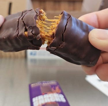 A hand breaks open a chocolate bar from Krack’d Snacks, revealing a gooey caramel-like center.