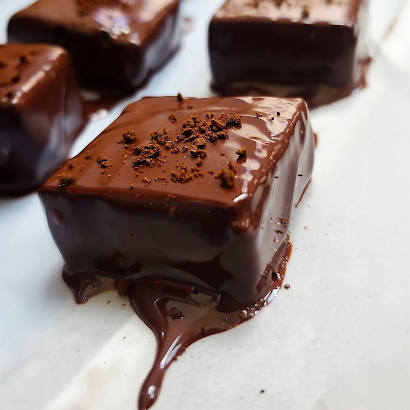 Close-up of Krack'd Snacks dark chocolate cubes with a glossy, melted coating and a sprinkle of cocoa powder.