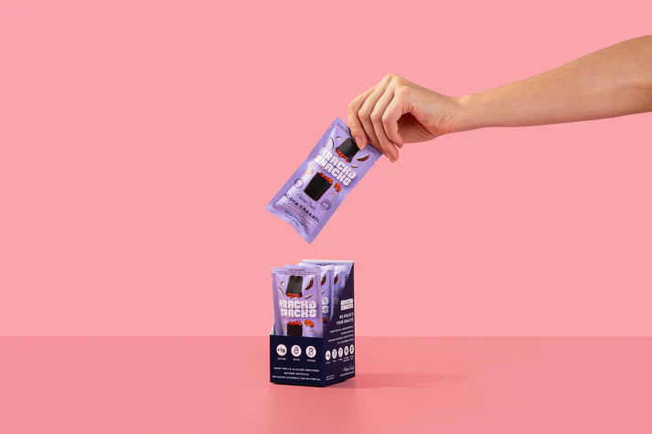A hand pulling a Krack’d Snacks Aloha Caramel bar from a tray, highlighting keto and low carb snacks.
